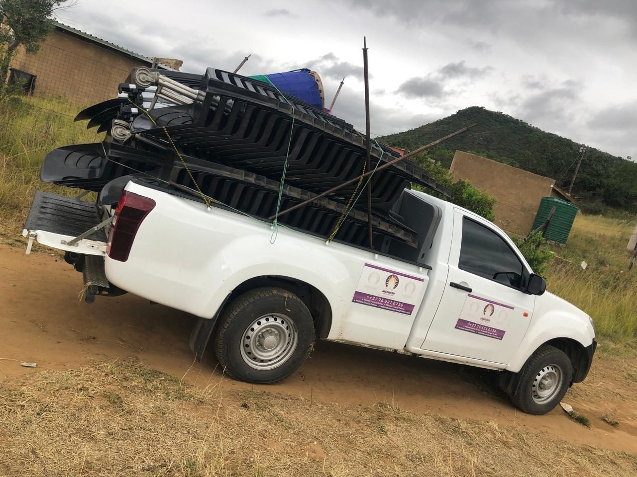 A branded vehicle loaded with stacked black chairs and tent poles on a rural dirt road.