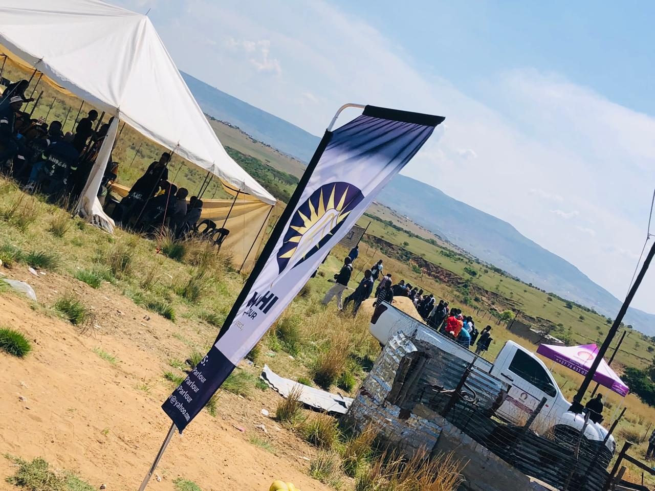 A white marquee, branded banner and vehicle set up on a hillside for a funeral service.
