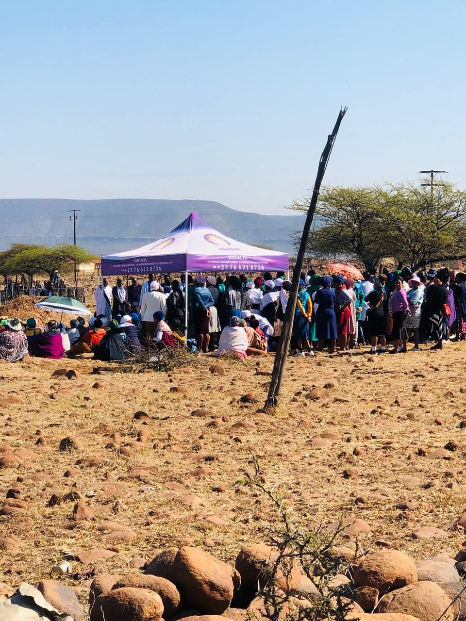 Mourners gathered around a purple and white branded canopy at a graveside service.