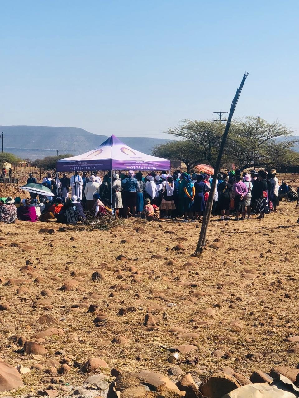 A large group of people gathered on open ground beside a branded Mshishi canopy.