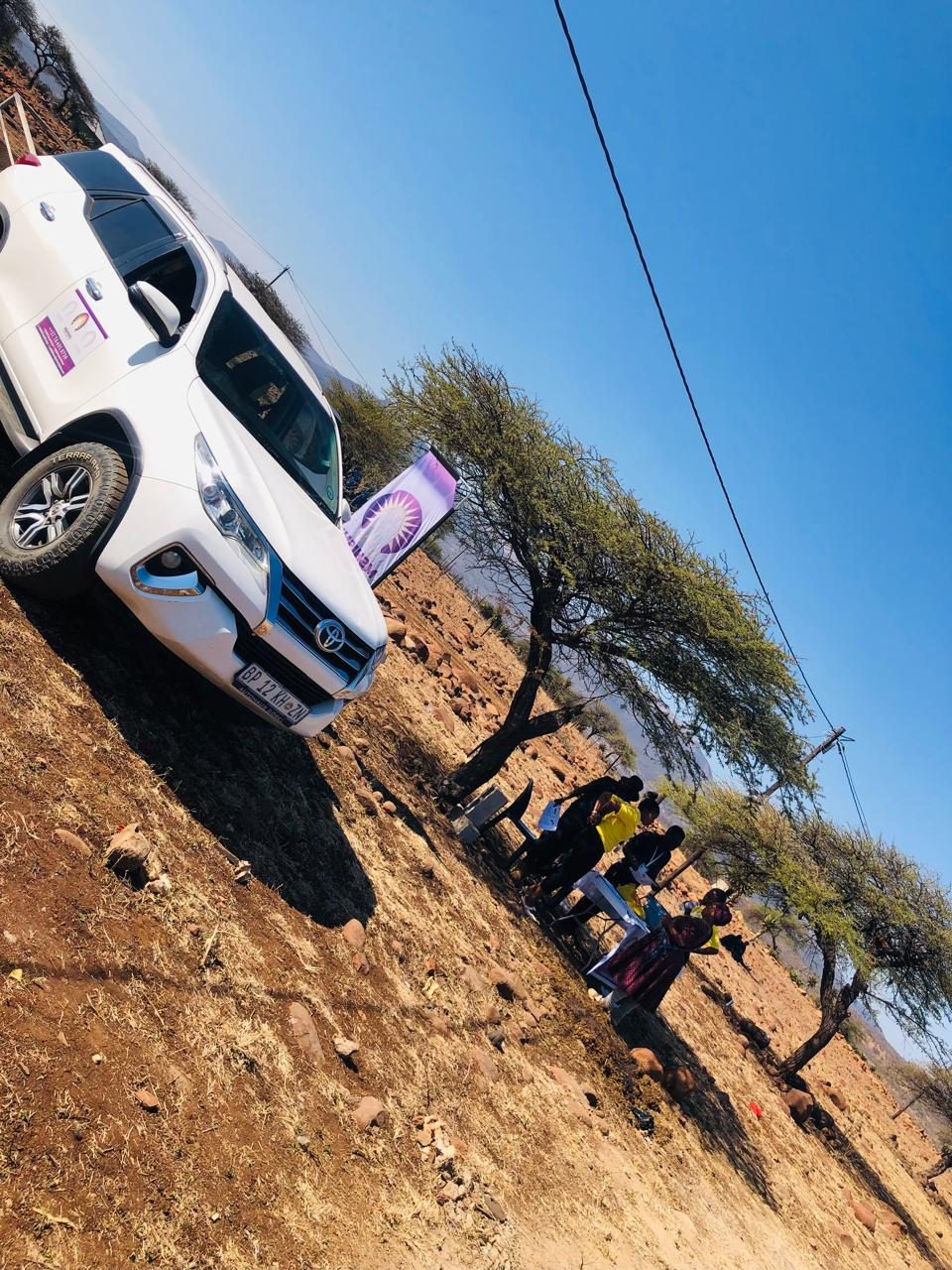 A branded Mshishi vehicle parked beside a purple banner stand at a rural service site.