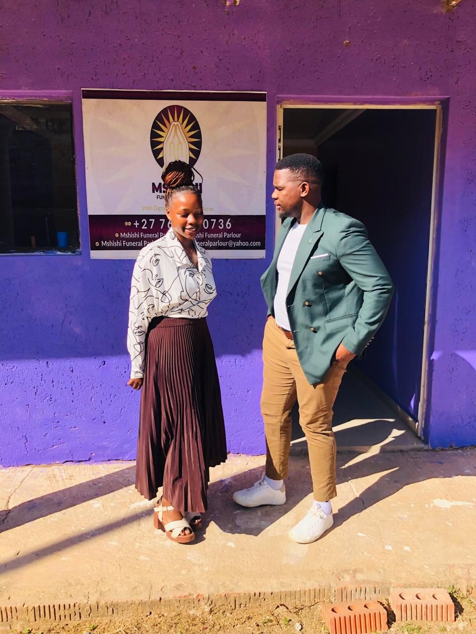 Two Mshishi team members standing in front of the office with its branded sign.